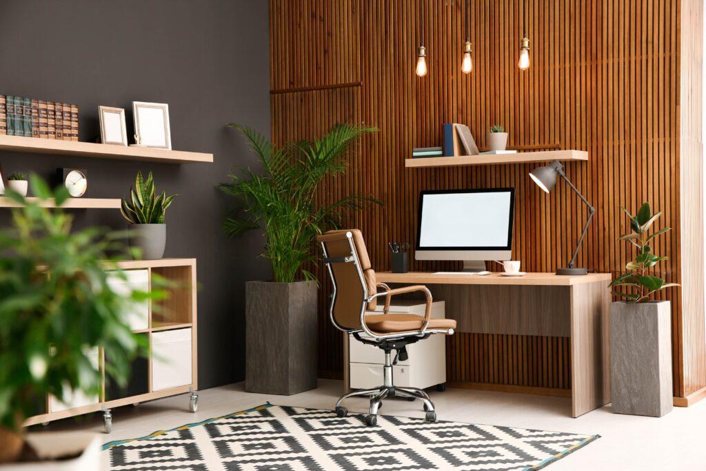 Bequemer Arbeitsplatz mit Computer in der Nähe einer Holzwand im stilvollen Innenraum. Home-Office-Design