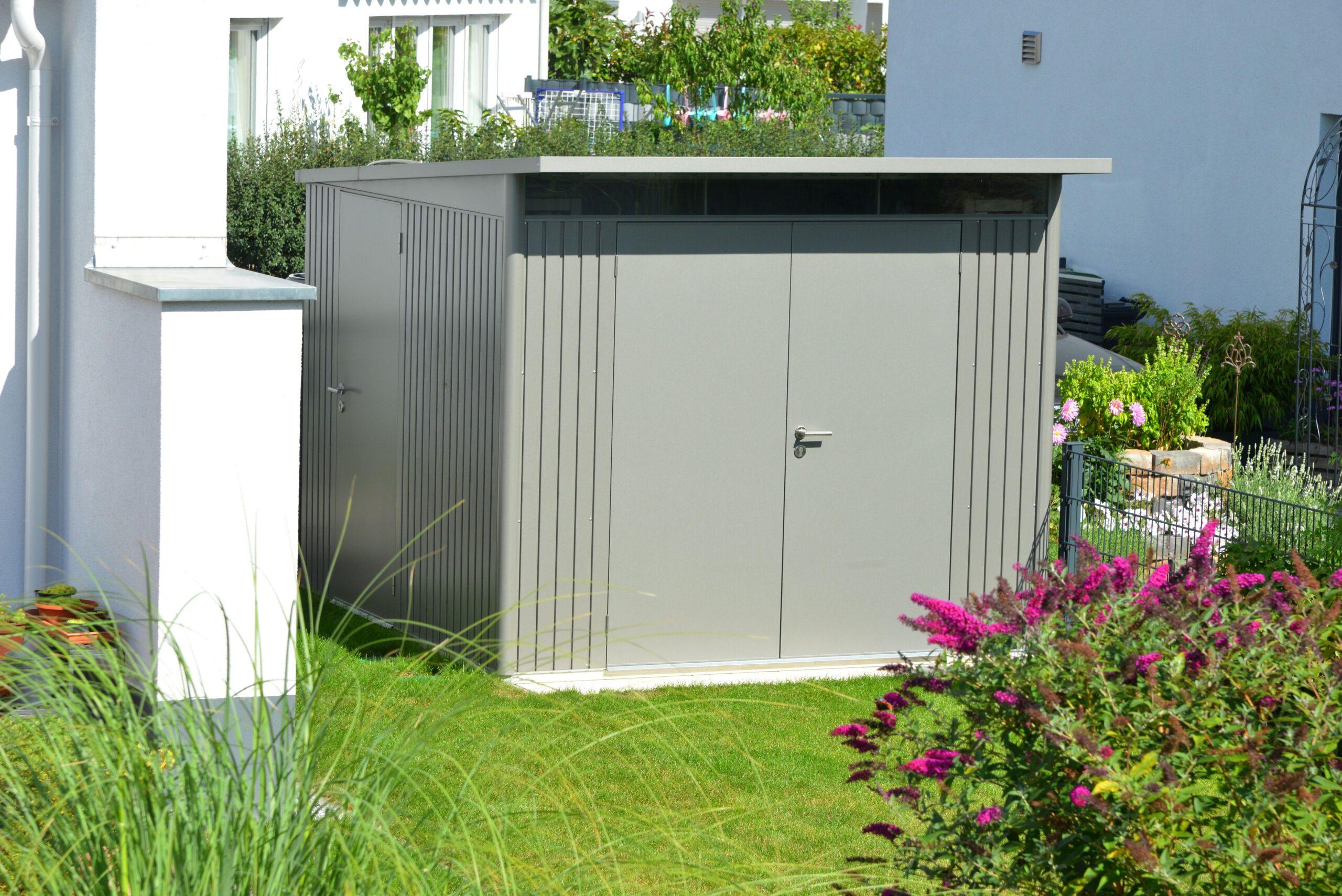 Moderne Mülltonnenverkleidung mit Flachdach in Grau vor gepflegtem Garten mit Blumen