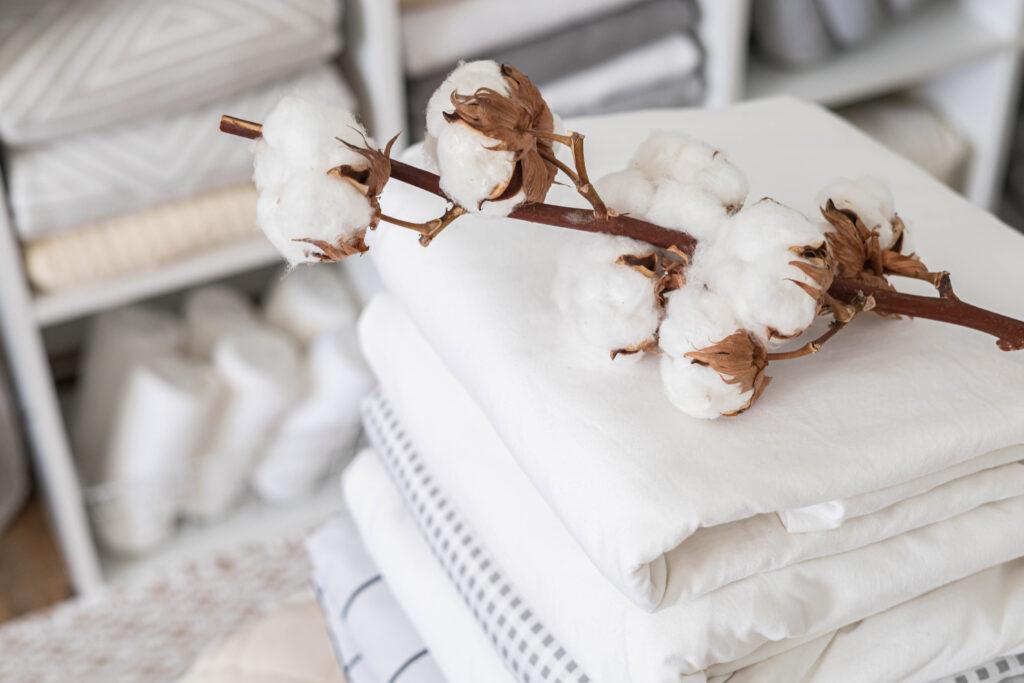 Alpaka Bettdecke liegt neben Baumwollzweig auf weisser Bettwaesche im Regal – Fokus auf Naturmaterialien im Schlafzimmer